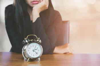 Woman wearing black top waiting by clock as a small featured image for blog post.