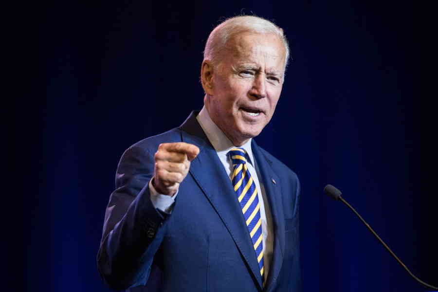 President Biden pointing at audience while wearing blue suit and tie.