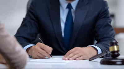 Man wearing suit and blue tie writing down interview responses on paper.